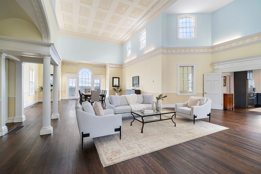Two-and-a-half-story great room at 66 Ocean Street with a balustraded mezzanine gallery, classical columns, marble fireplace, and tall Palladian windows opening to the ocean