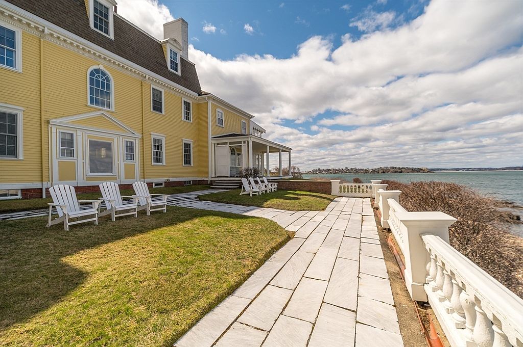 Oceanfront terrace at 66 Ocean Street with a stone balustrade, bluestone walkway, and Adirondack chairs on the lawn beside the yellow house, water beyond