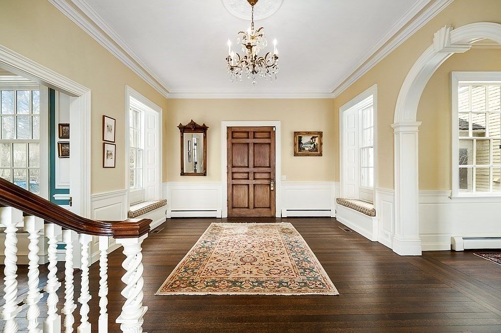 Entrance foyer with a crystal chandelier, a paneled six-panel door, arched openings, white wainscot, and an antique runner on dark hardwood