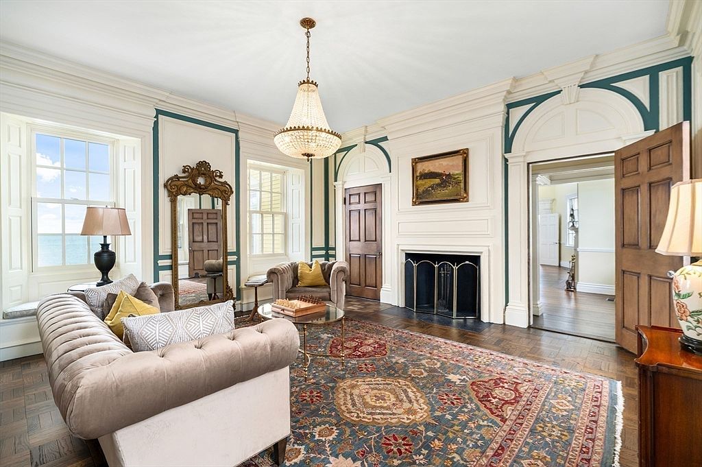 Formal parlor with green-trimmed raised paneling, a marble fireplace, gilt mirror, chesterfield sofas, and tall windows looking out to the ocean