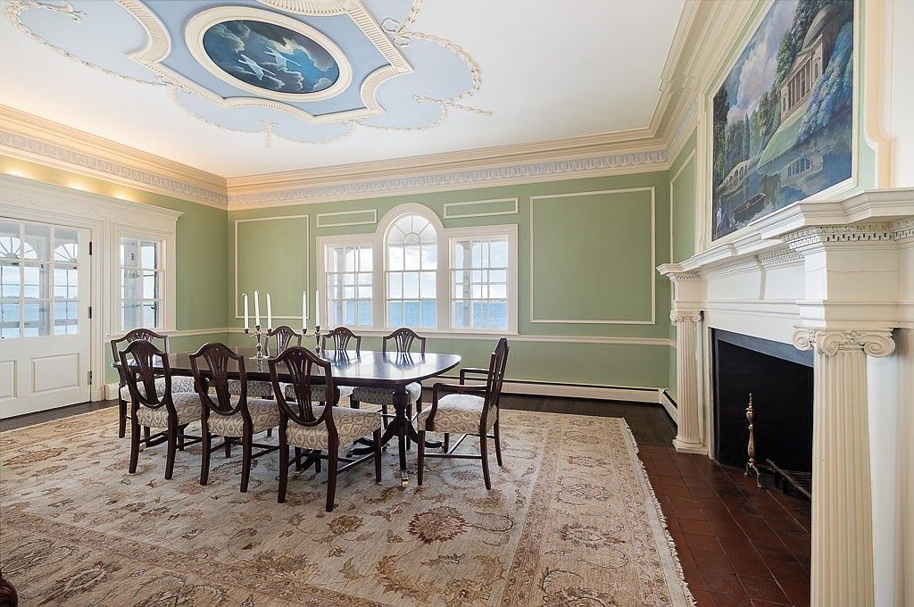Formal dining room with sage-green panel walls, a painted sky ceiling medallion, arched Palladian windows over the water, and a classical fireplace