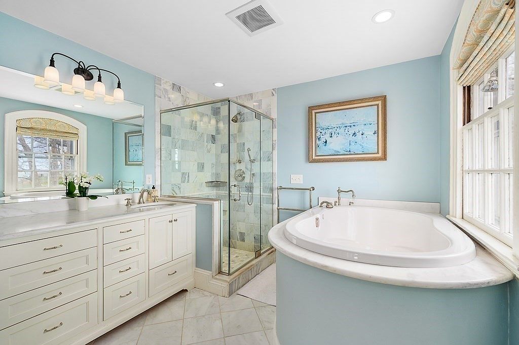 Primary bathroom with pale blue walls, a marble-tiled glass shower, a freestanding oval soaking tub, and a double white vanity