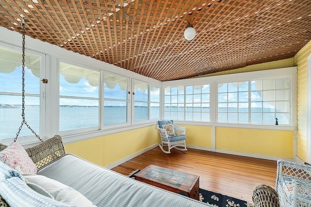 Upper sleeping porch with a woven lattice ceiling, yellow wainscot, a hanging daybed swing, and windows on multiple sides framing the water