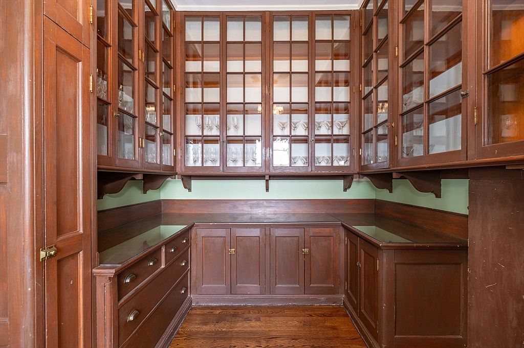Butler's pantry lined floor to ceiling with glass-front mahogany cabinetry holding period glassware, with paneled lower cabinets and counters